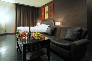 A hotel room with a bed, a leather sofa, a glass coffee table with flowers, and wall art.