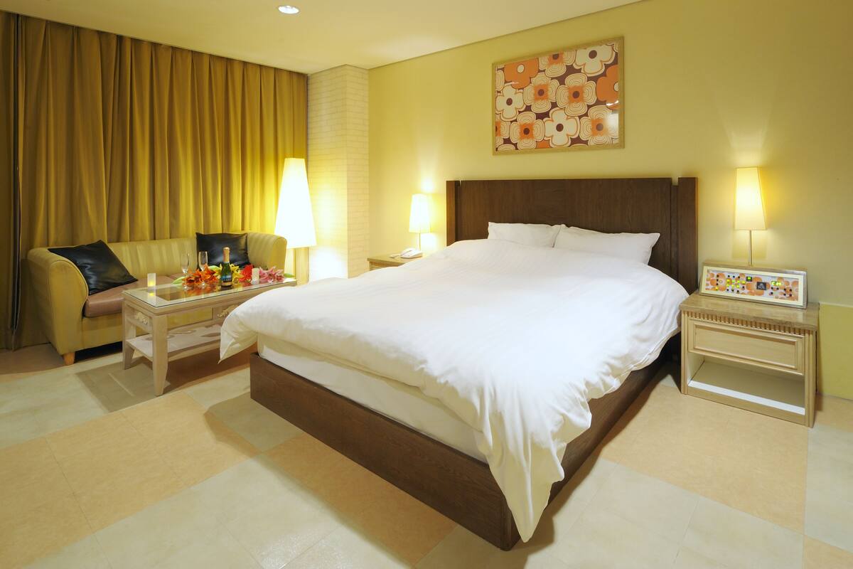 A hotel room with a large bed, a sofa, two bedside tables with lamps, and a decorative wall piece.