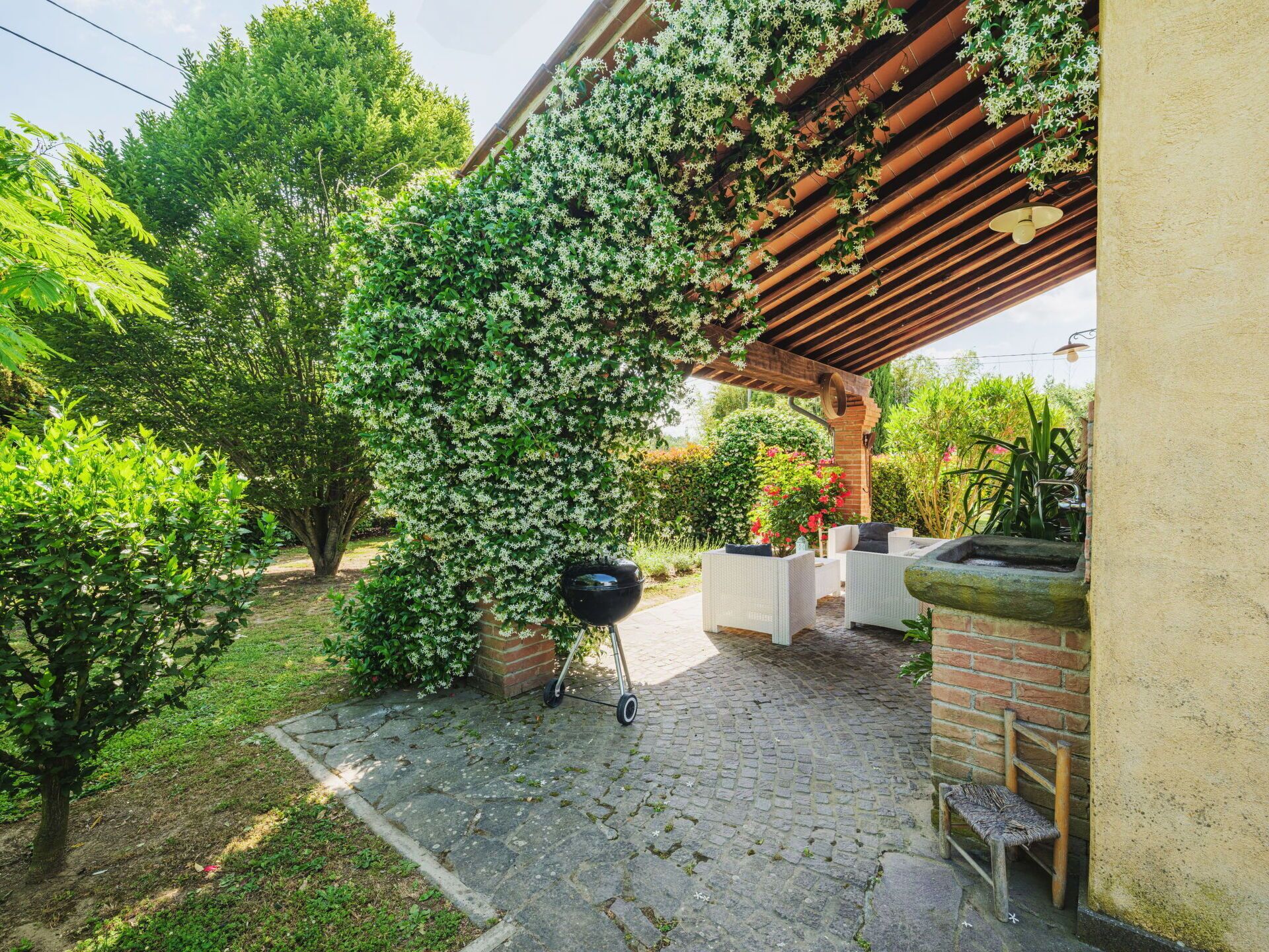 Eine Terrasse mit Pergola, Gartenmöbeln und Grill.