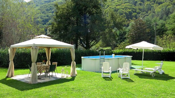 A gazebo with a table and chairs, a swimming pool, and lounge chairs in a grassy area with a mountain backdrop. - Beautiful apartment for 6 guests with hot tub, WIFI, pool, TV and patio (Casoli)