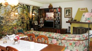 En stue med spisebord, blomstret sofa, bogreol og pejs.