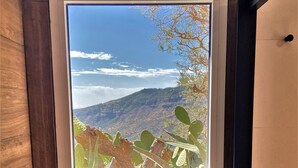 Une fenêtre donnant sur un paysage montagneux et une végétation clairsemée.