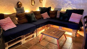 Un salon chaleureux avec un canapé d’angle, de nombreux coussins, une table basse en bois et des chapeaux accrochés au mur.