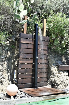 Una fuente de madera con un caño vertical, rodeada de rocas y plantas.