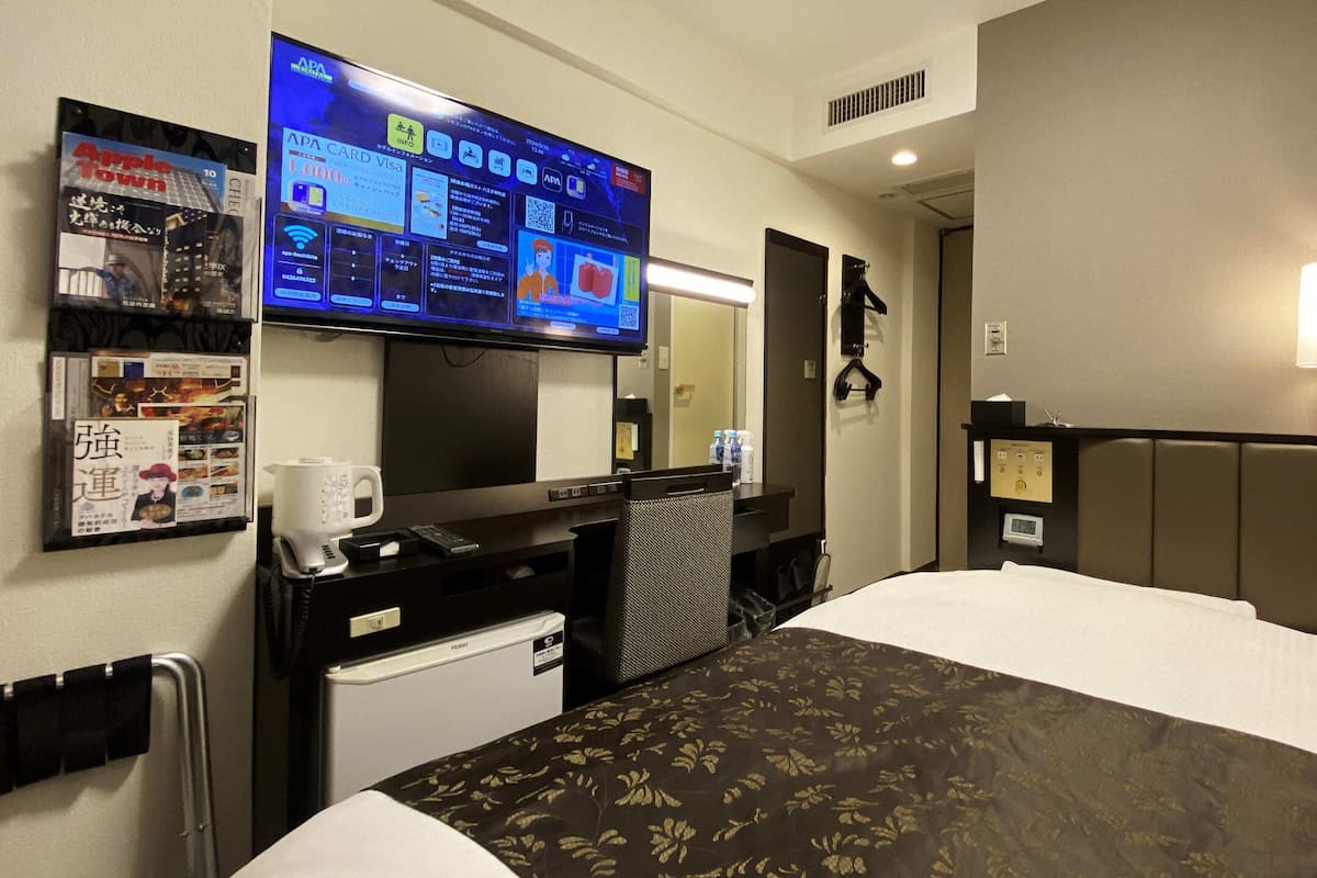A hotel room with a bed, a desk with a computer, a television, and a minibar.