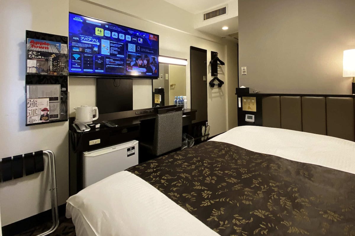 A hotel room with a bed, a desk with a computer, a television, and a mirror.