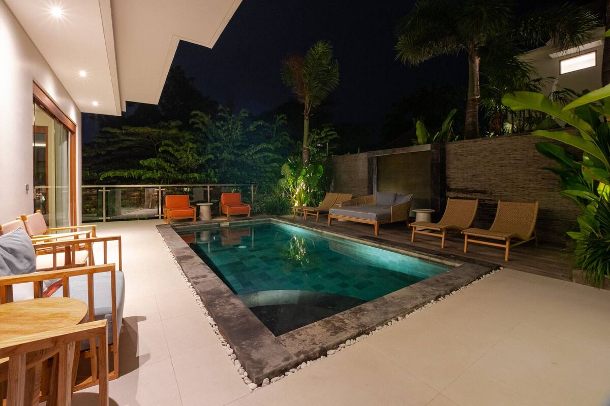 Un área de piscina exterior moderna con sillones de descanso y una mesa de comedor.