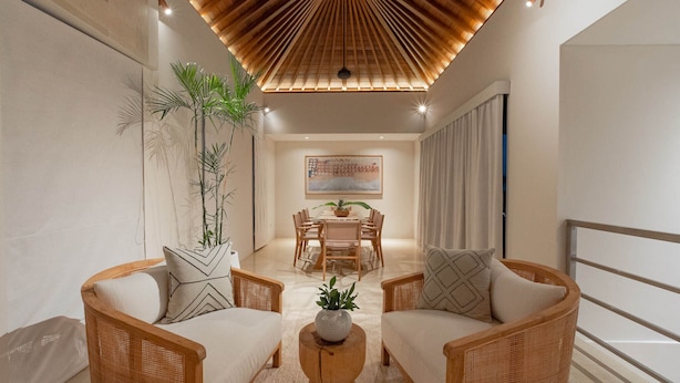 Un salon moderne avec des meubles en osier, un plafond en bois et un coin repas à l’arrière-plan.