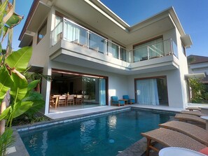 Une maison moderne à deux étages, dotée d’une piscine, d’un espace salon extérieur et d’un balcon.
