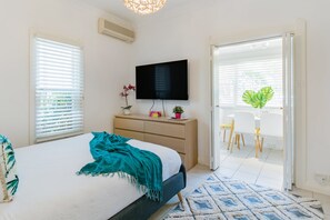 A bedroom with a bed, a TV, a dresser, and a dining area with chairs and a table.