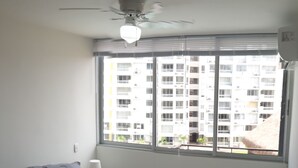 A bedroom with a bed, a ceiling fan, a window with a view of a building, and a nightstand with a lamp. - Comfort, NATURE, REST AND FUN WITH THE FAMILY (RICAURTE CUNDINAMARCA)