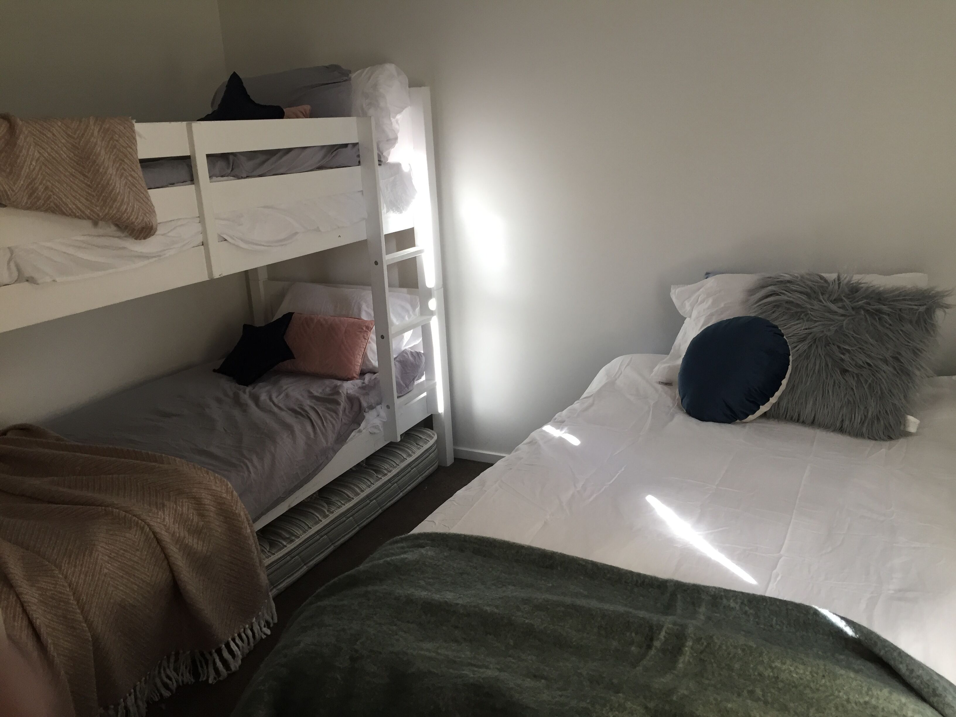 A dorm-style room with bunk beds, a single bed, and a window providing natural light.
