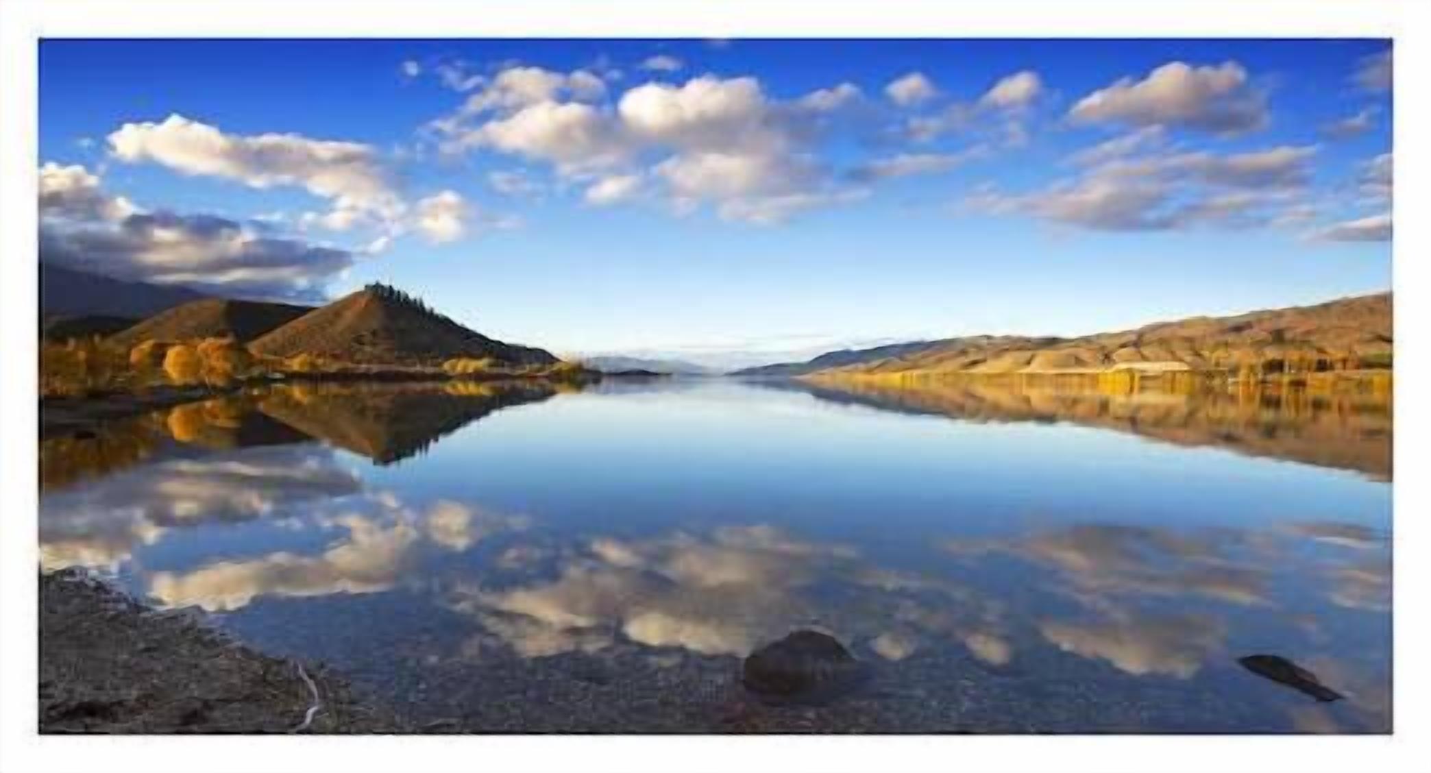 A calm lake with mountains in the background and a clear sky.