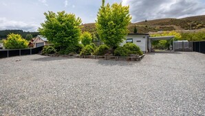 A gravel driveway leading to a house with a covered porch and a small garden area with trees and shrubs. - Clyde Gem (Clyde)