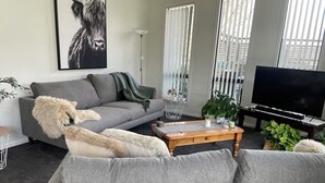 A living room with a grey sofa, a wooden coffee table, a television, and a large window with blinds. - Clyde Gem (Clyde)