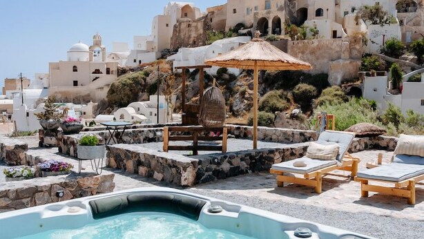 Ein Whirlpool mit Liegestühlen und einer Holz-Pergola, umgeben von weißen Gebäuden mit Kuppeldächern.