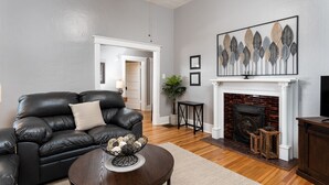 Una sala de estar con un sofá de cuero negro, una mesa redonda de centro, una chimenea y una obra de arte enmarcada en la pared.