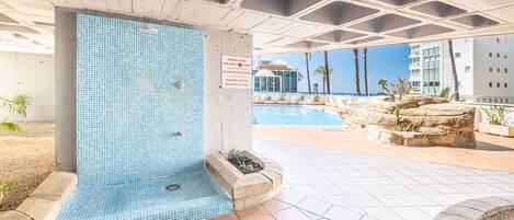 A swimming pool area with a tiled wall, a sign indicating pool hours, and a view of a building in the background.