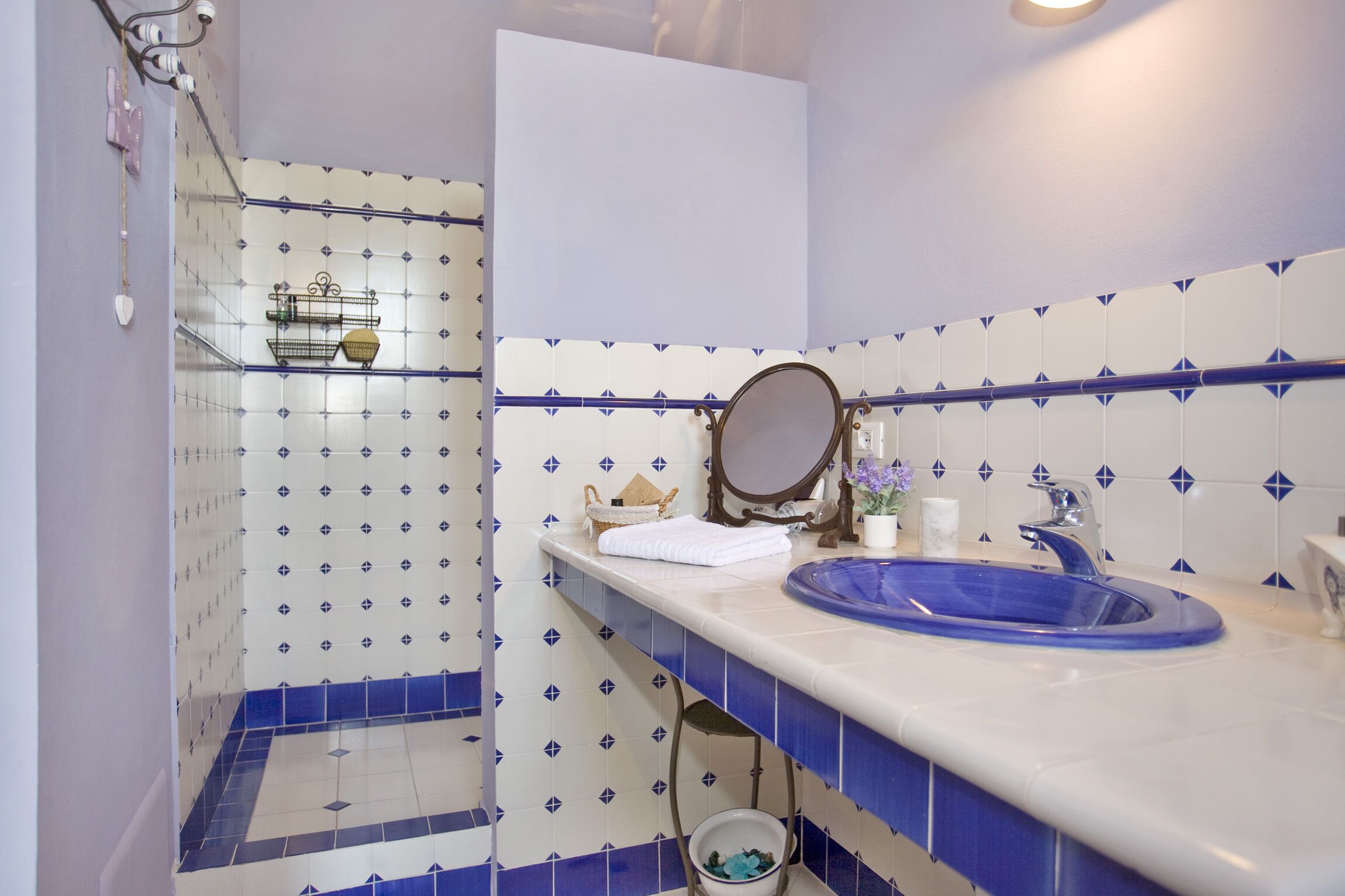 Een badkamer met een blauw-wit betegeld design, een wastafel met een blauwe kom, een spiegel en een douchegedeelte met een blauw-witte betegelde wand.