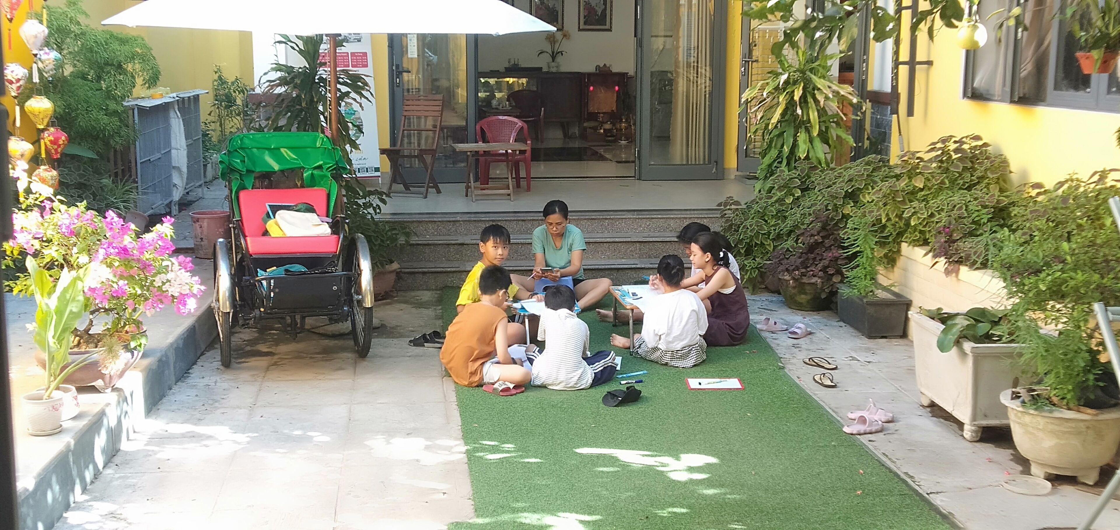 A courtyard with a green artificial turf, potted plants, and a red and green cart.