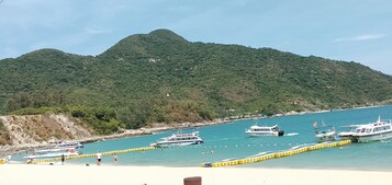 Una zona costera con barcos amarrados cerca de la orilla, una playa de arena y una colina al fondo.