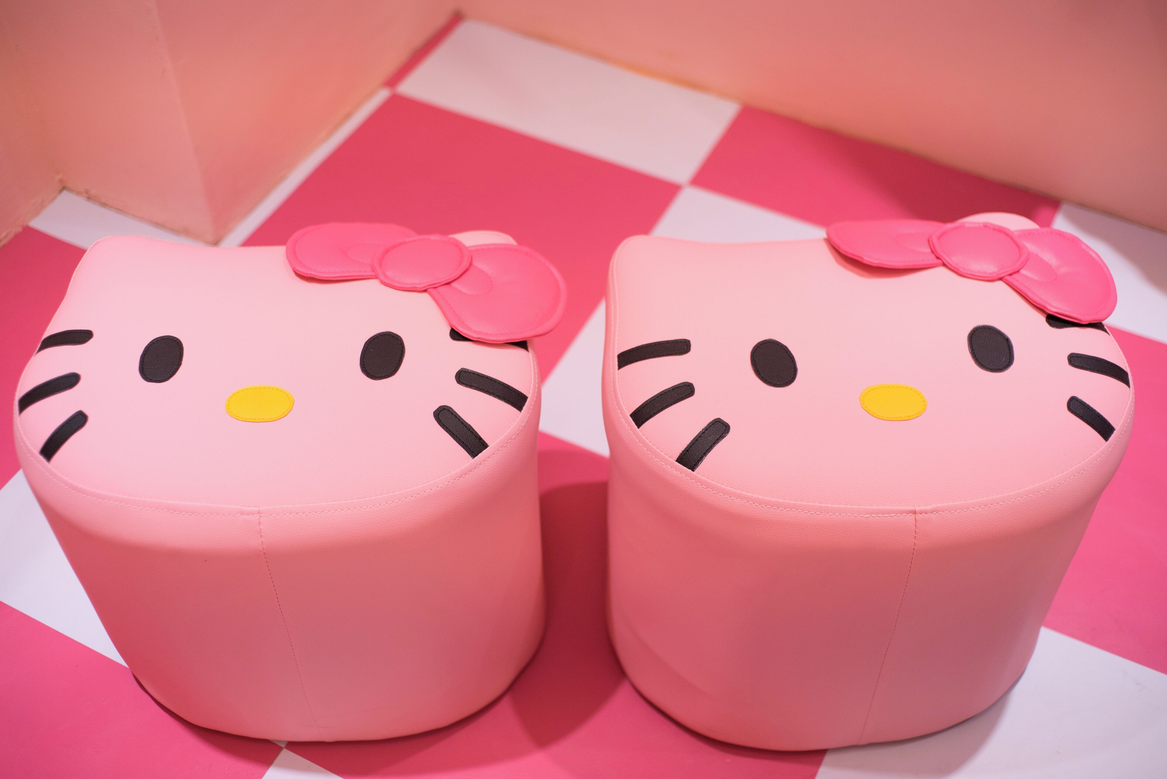 Two pink Hello Kitty ottomans with bows on a pink and white checkered floor.