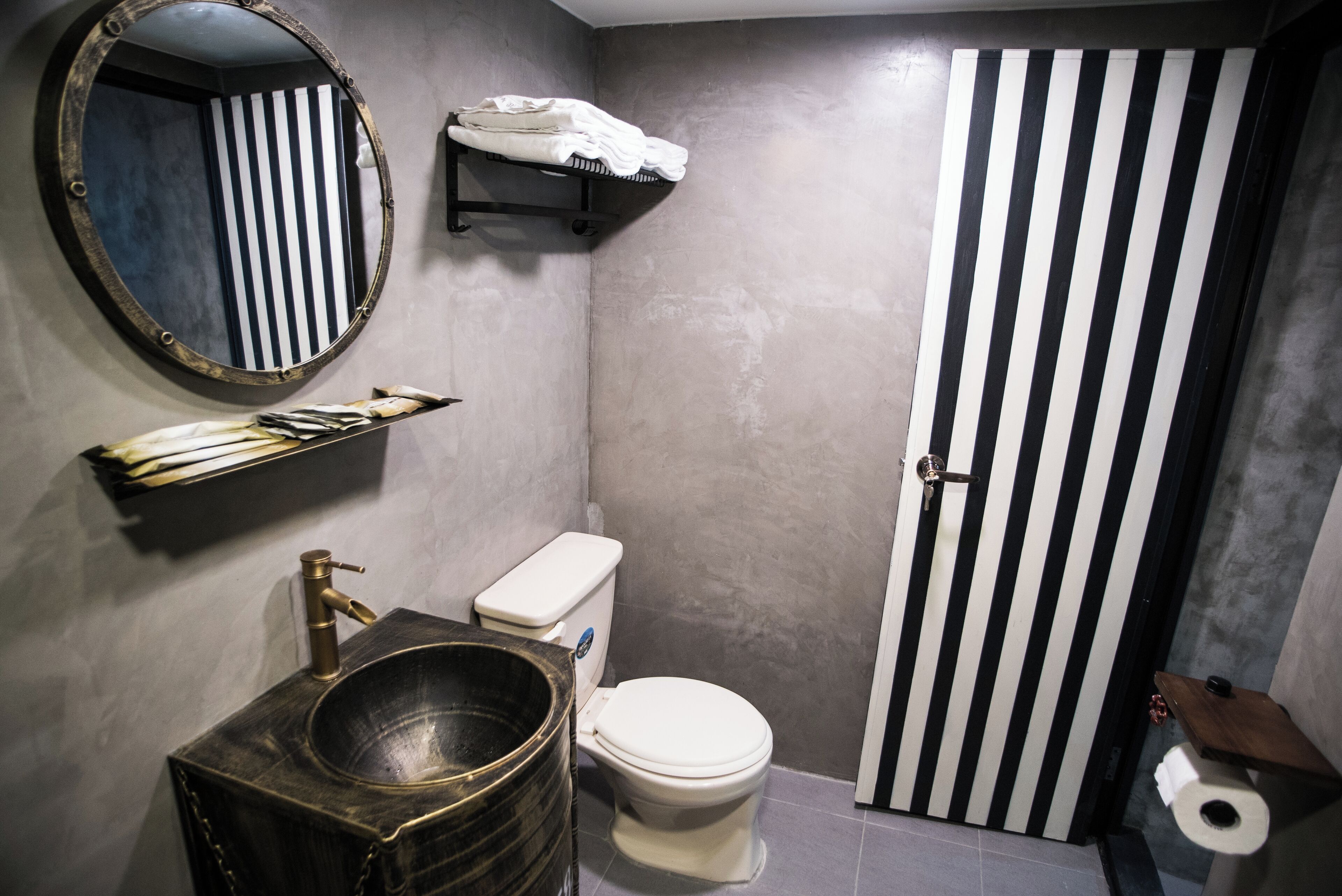 A bathroom with a round mirror, a wooden sink, a toilet, and a striped door.