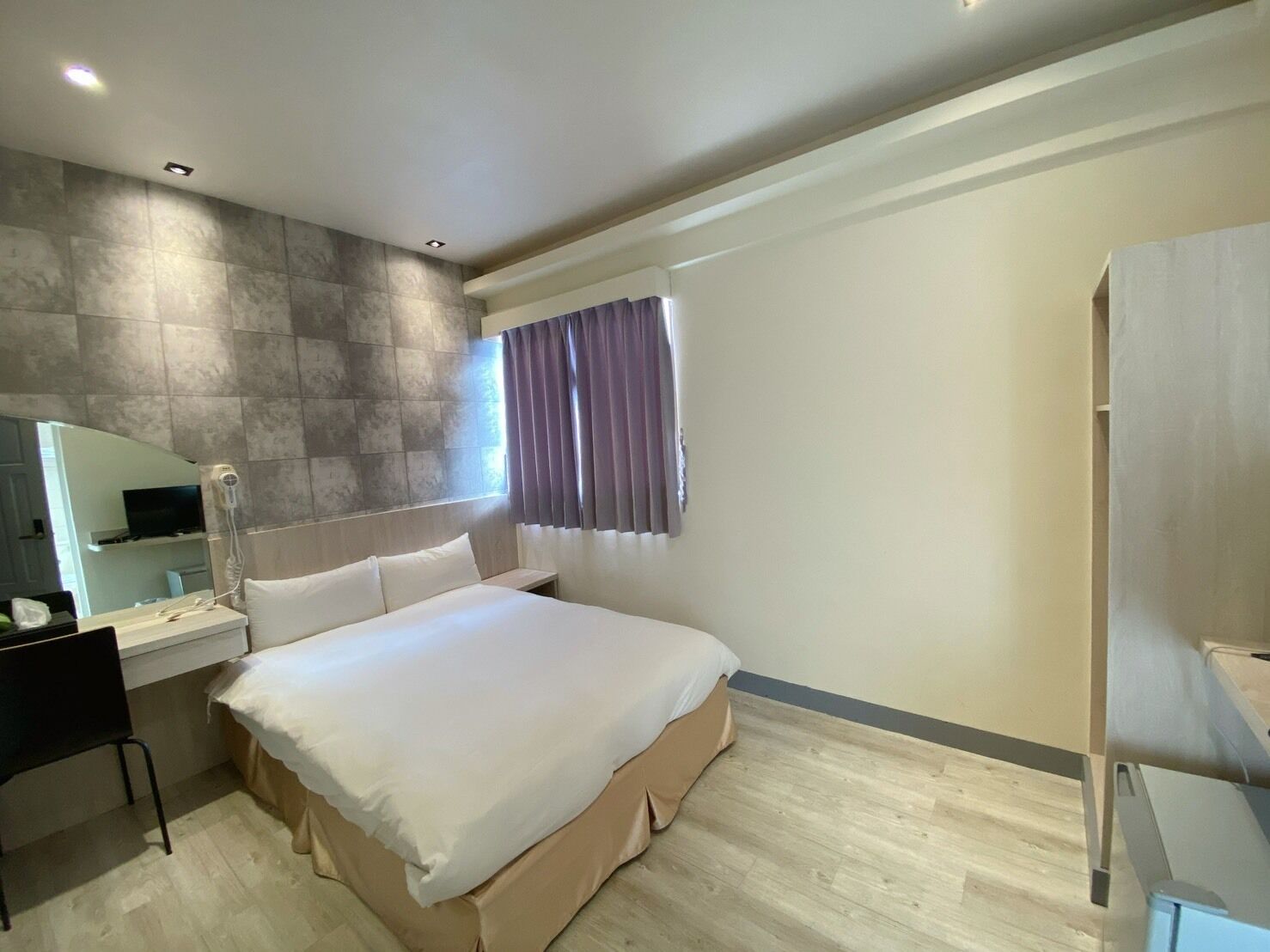 Una habitación de hotel moderna con una cama grande, un escritorio con silla, un espejo y una ventana con cortinas.