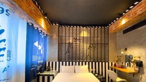 A hotel room with a bed, a desk, and a chair. There is a window with bars, and a wall-mounted rack with keys. - Hexing Hotel (Magong)