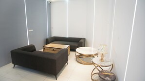 A modern living room with a dark sofa, a wooden coffee table, a round glass table with a white marble top, and a small stool. - Hexing Hotel (Magong)
