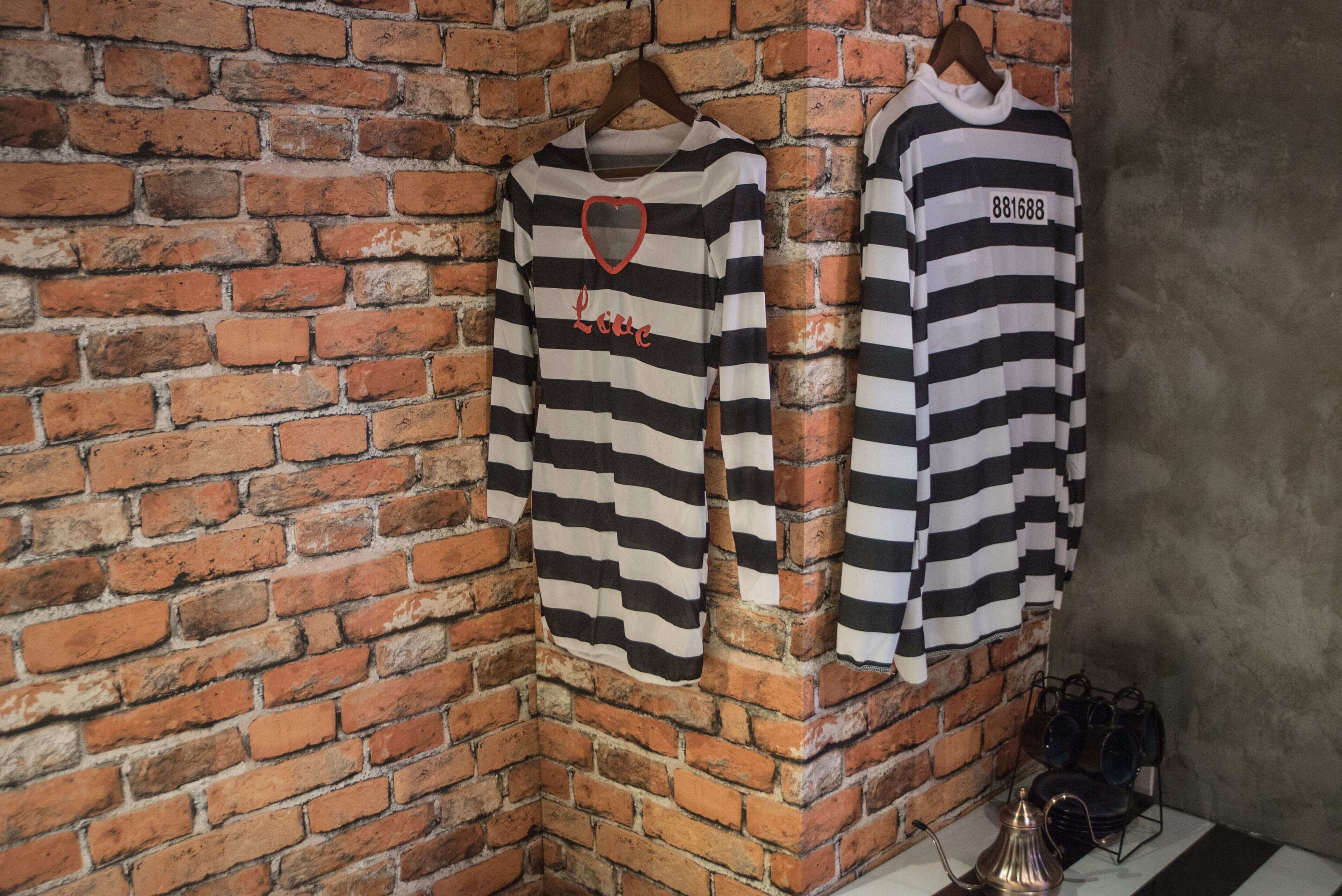 Two striped shirts hanging on a brick wall.