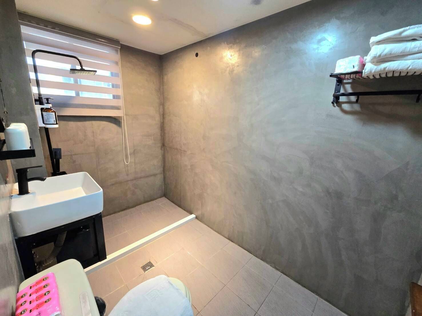 Un baño con ducha, lavabo e inodoro. Hay toallas en un perchero y una botella de jabón de manos sobre el lavabo.