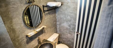 Casa de banho com espelho redondo, sanita, lavatório e porta riscada.