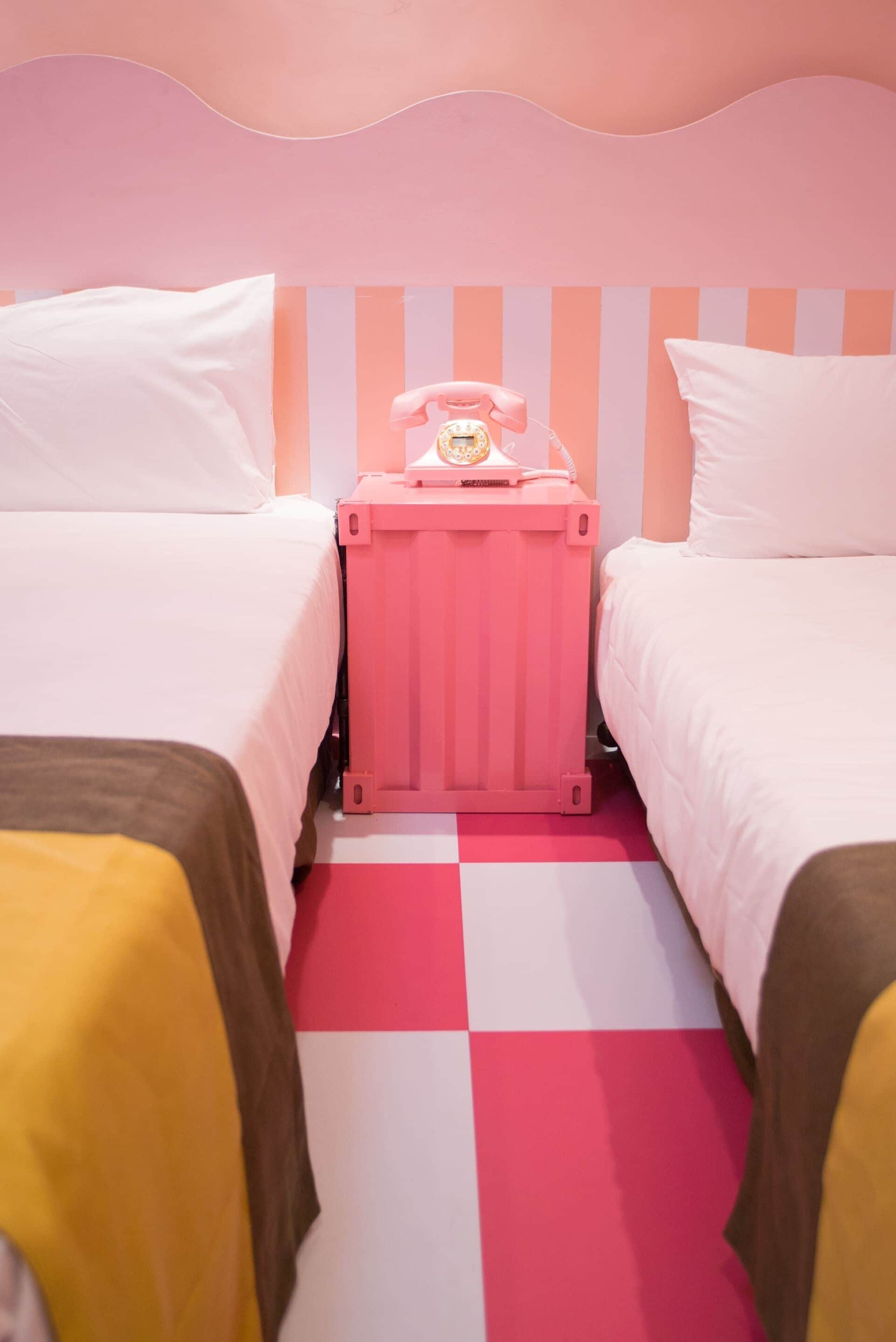 A hotel room with two beds, a pink suitcase, and a telephone on the nightstand.
