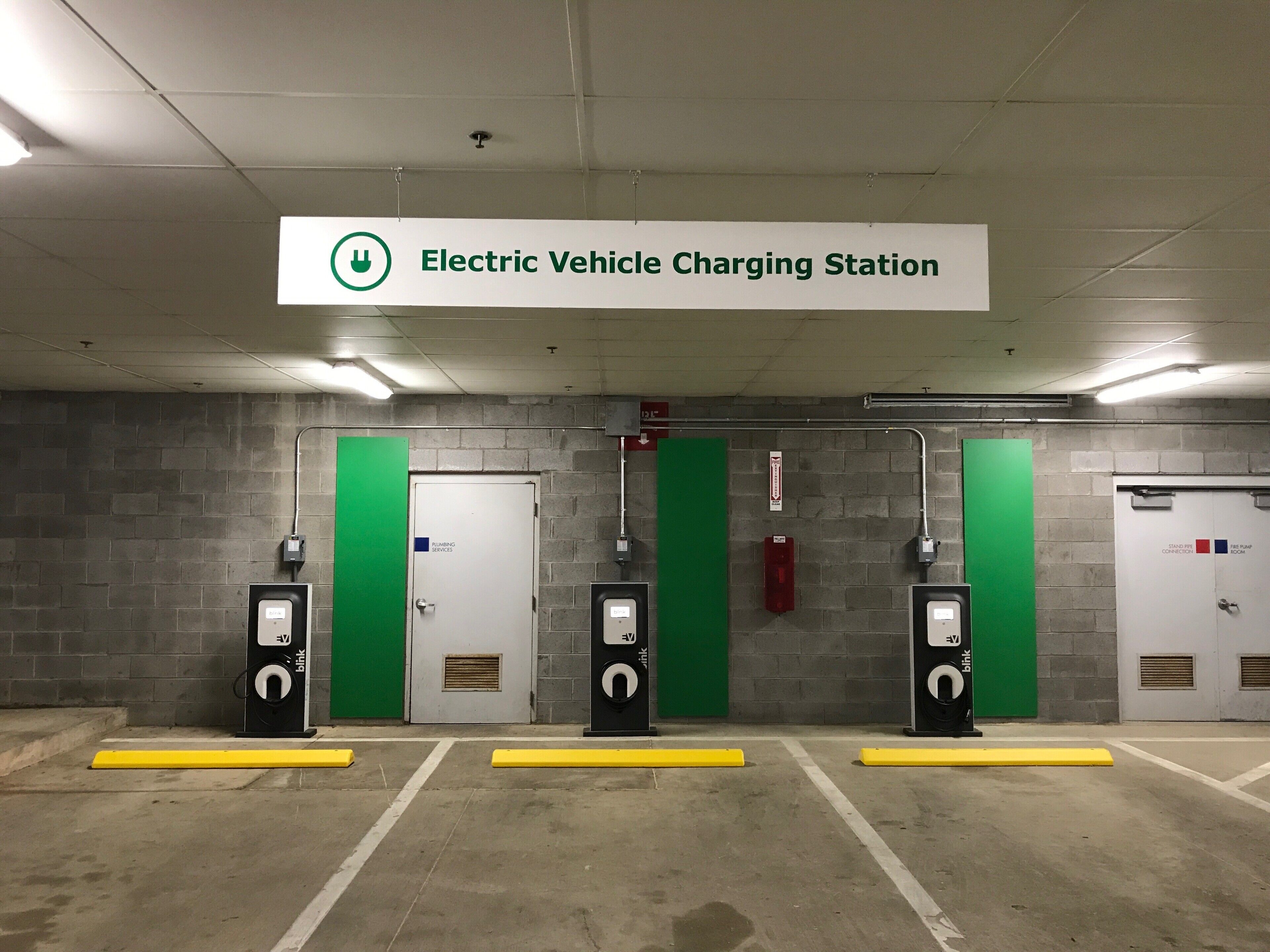 An electric vehicle charging station with three charging points, a sign indicating the station, and a fire safety connection room.