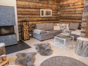 Ein gemütliches Blockhaus-Interieur mit Kamin, grauem Sofa und rustikalem Dekor.