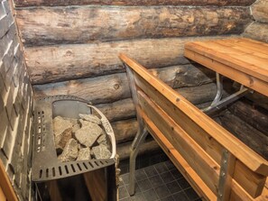 Eine hölzerne Bank und ein Metallgrill mit Steinen im Inneren, vor rustikalen Holzwänden.