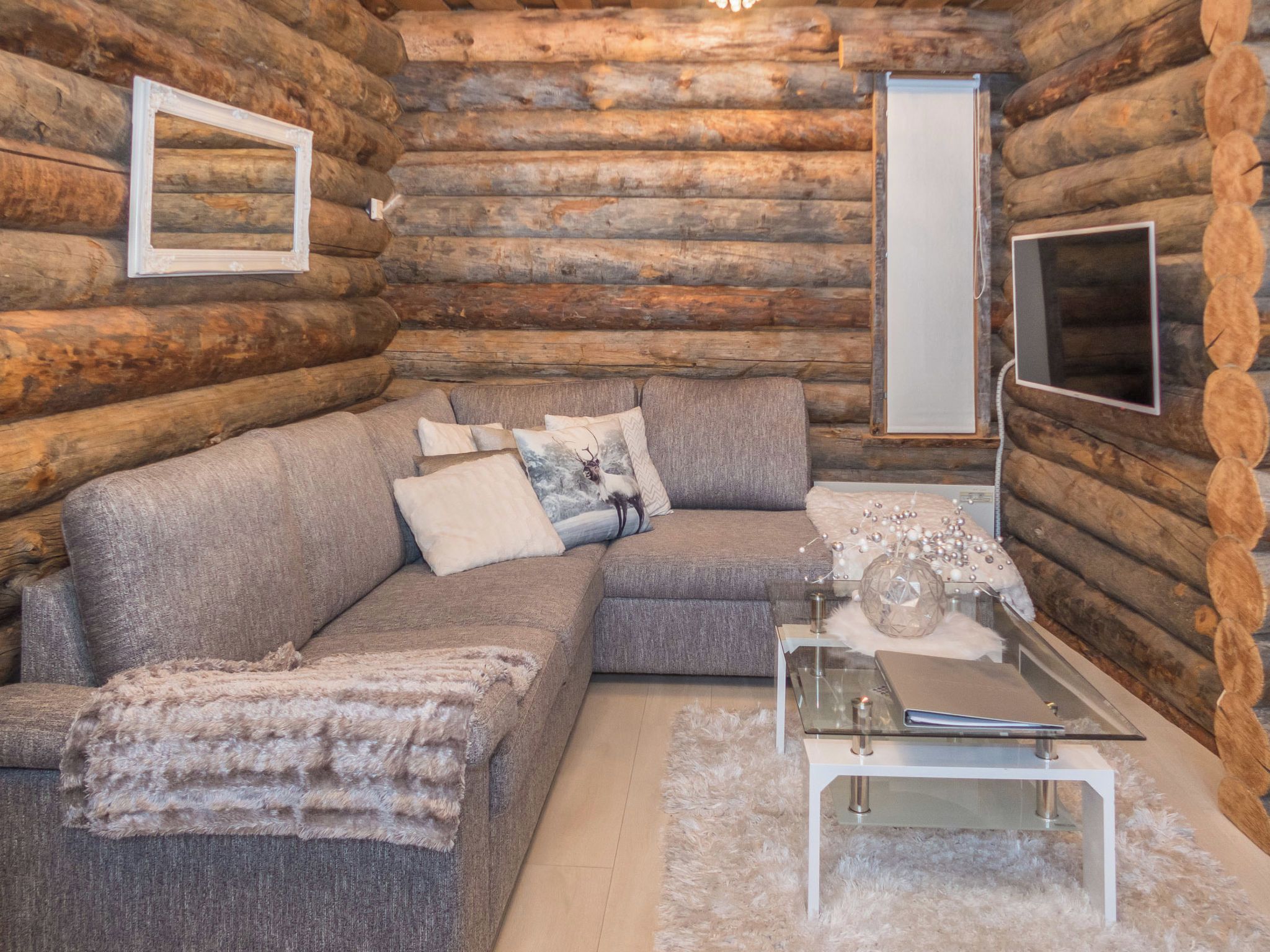 A log cabin interior with a sectional sofa, a glass coffee table, and a television.