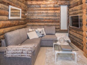 A log cabin interior with a sectional sofa, a glass coffee table, and a television.