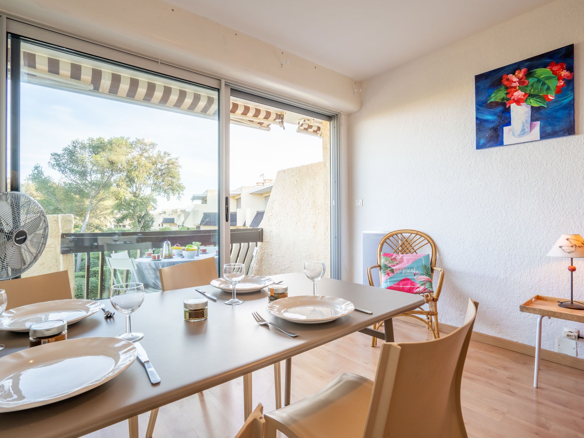 A dining area with a table set for four, a wicker chair, and a view of the outdoors.