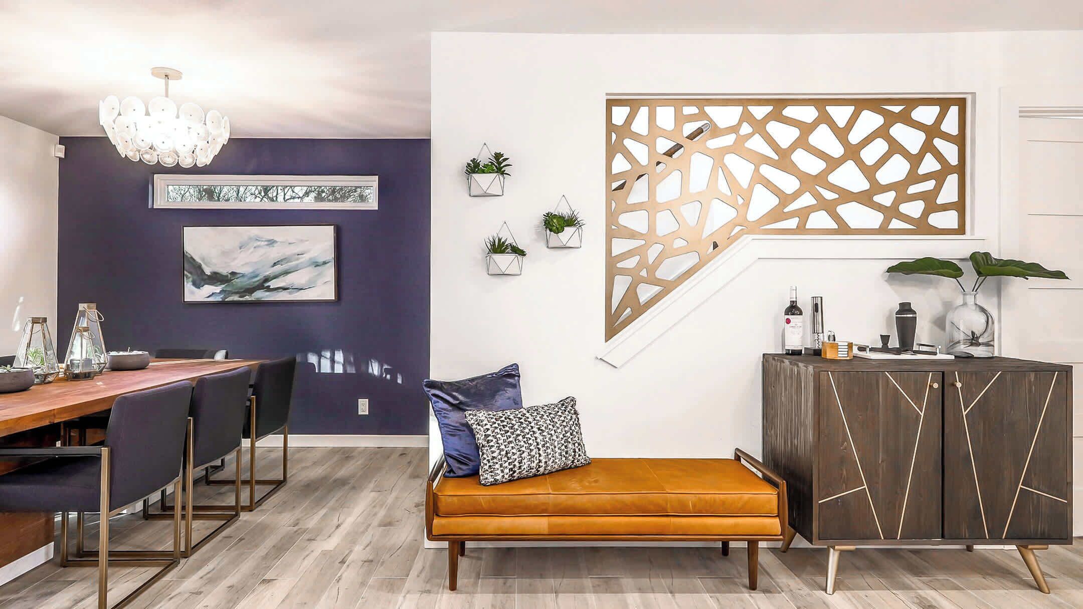 Un espace de salle à manger moderne avec une table en bois, des chaises, un banc, un lustre, des œuvres d’art murales et un élément de séparation décoratif.