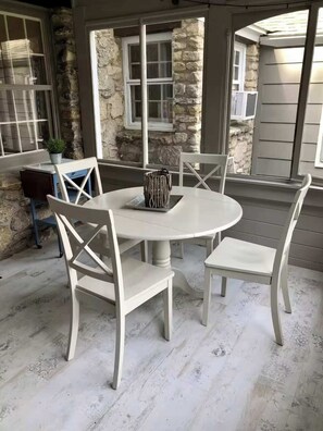 A round table with four white chairs, a stone wall, and a window with blinds. - Manistique Stone Cottage - Next to Peninsula State Park (Fish Creek)