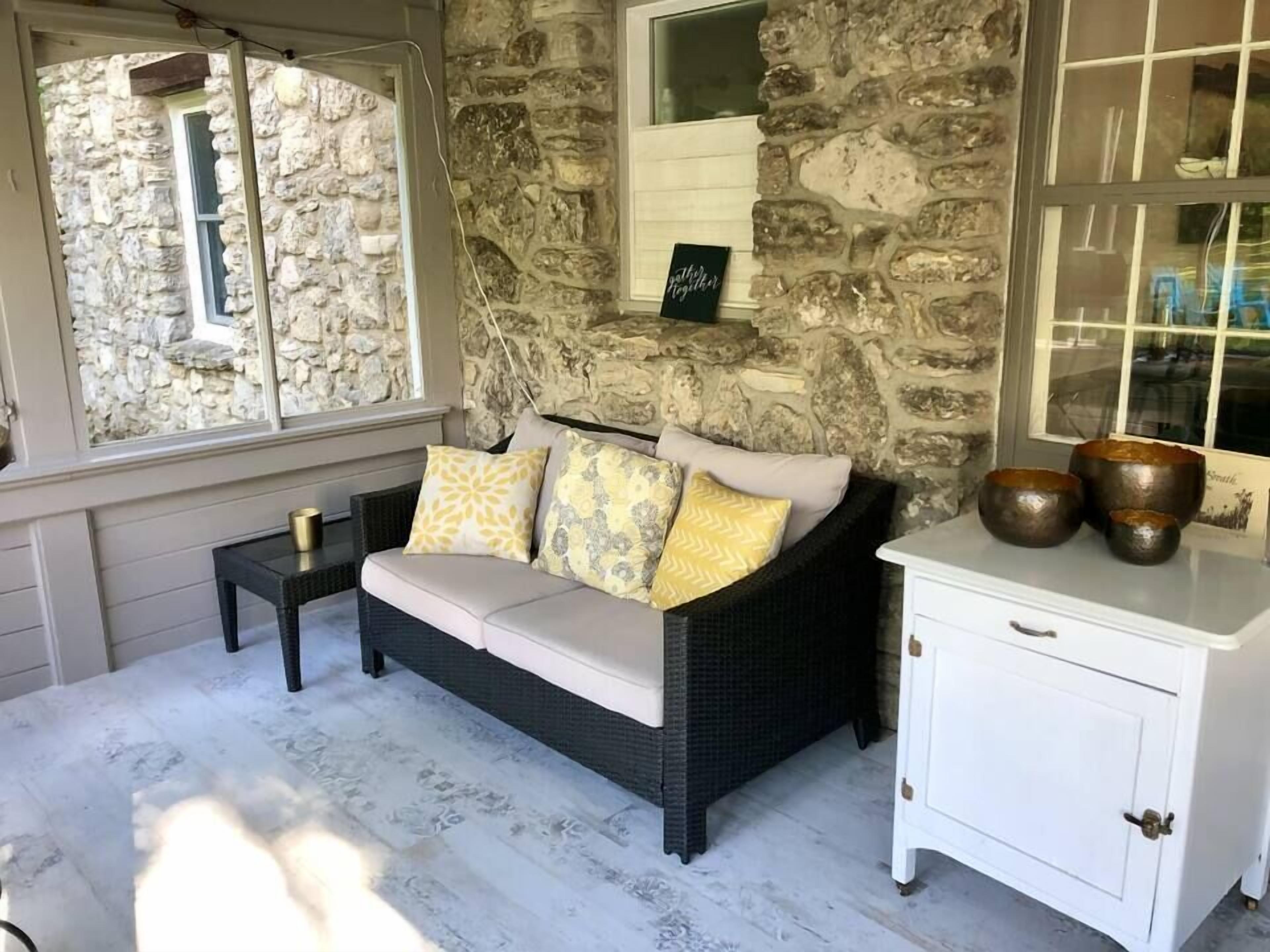A stone wall, a wicker sofa with cushions, a small table with a cup, and a white cabinet with handles.
