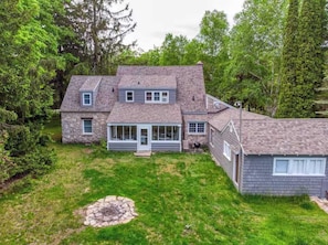 A two-story house with a stone exterior, a covered patio, and a stone fire pit in the yard.
