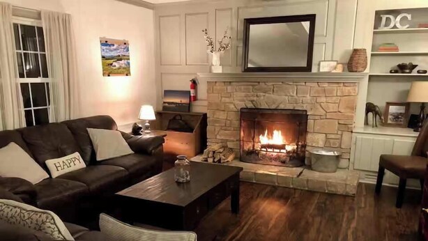 Una sala de estar con chimenea de piedra, sofás de cuero, una mesa de centro y un televisor sobre la chimenea.