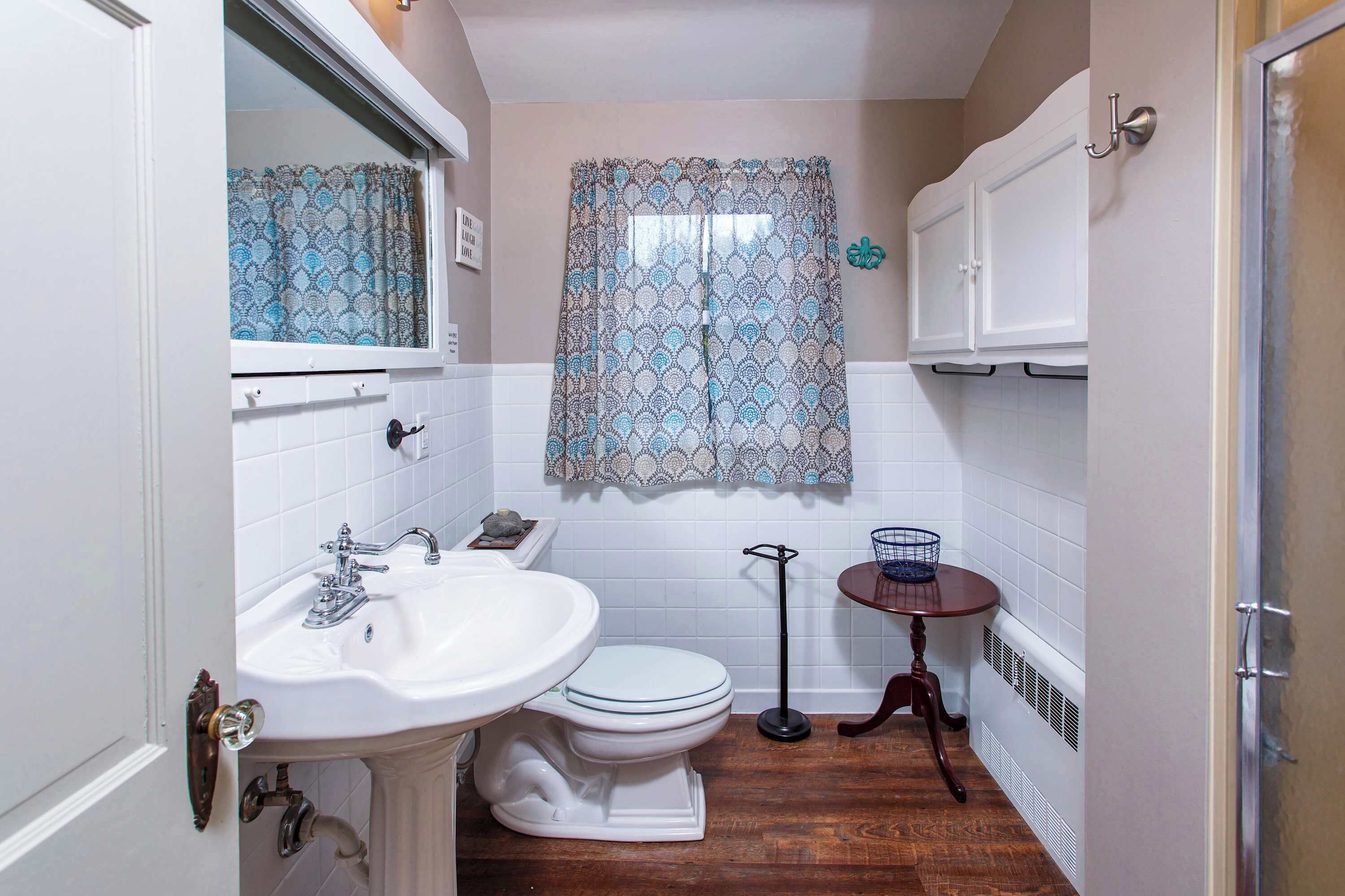 Un baño con lavamanos, inodoro y una ventana con cortinas estampadas.