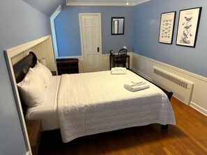 A bedroom with a bed, a nightstand, a chair, a radiator, and framed artwork on the wall. - Manistique Stone Cottage - Next to Peninsula State Park (Fish Creek)