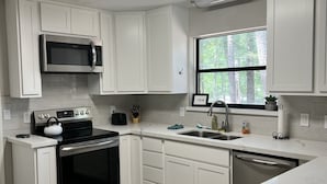 Cocina moderna con armarios blancos, electrodomésticos de acero inoxidable y un amplio ventanal con vista a árboles.