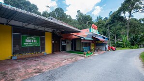 A motel with a green signboard, a red car parked outside, and a road in the foreground. - OYO 89921 Motel New Bay Sg. Lembing (Sungai Lembing)
