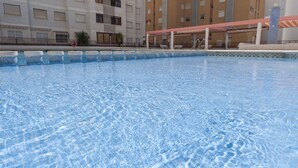 A swimming pool with clear blue water, surrounded by a tiled deck and a covered area with a red roof. - NAVEGANTE - Apartment with shared pool in Playa de Gandia. (Playa de Gandia)